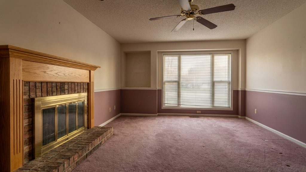 Dated living room with mauve carpet, brass fireplace, and ceiling fan