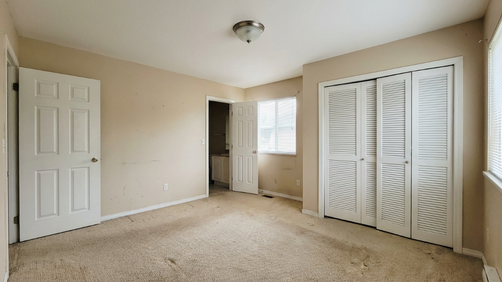 Plain beige bedroom with worn carpet and louvered closet doors