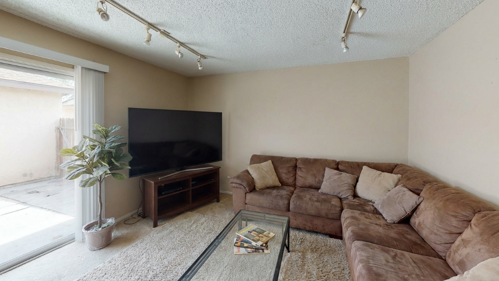 Dated living room with brown sectional sofa, glass coffee table, and track lighting